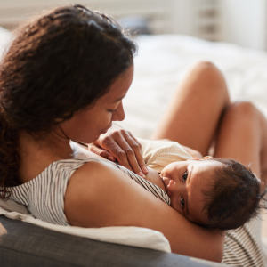 A woman is bre4astfeeding a baby reclined on a bed